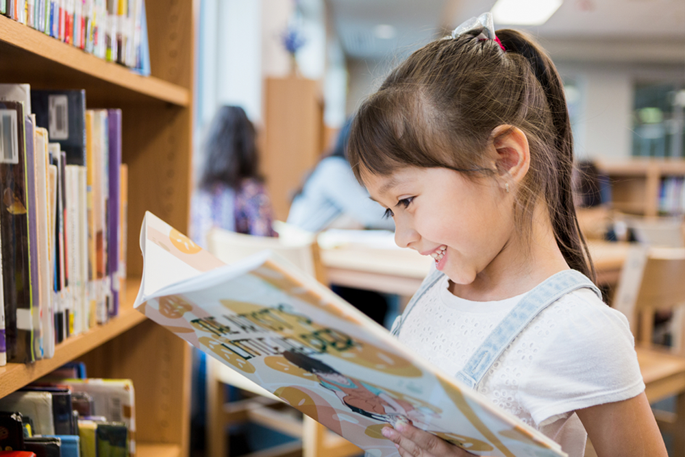 happy elementary student reading a book in the school library