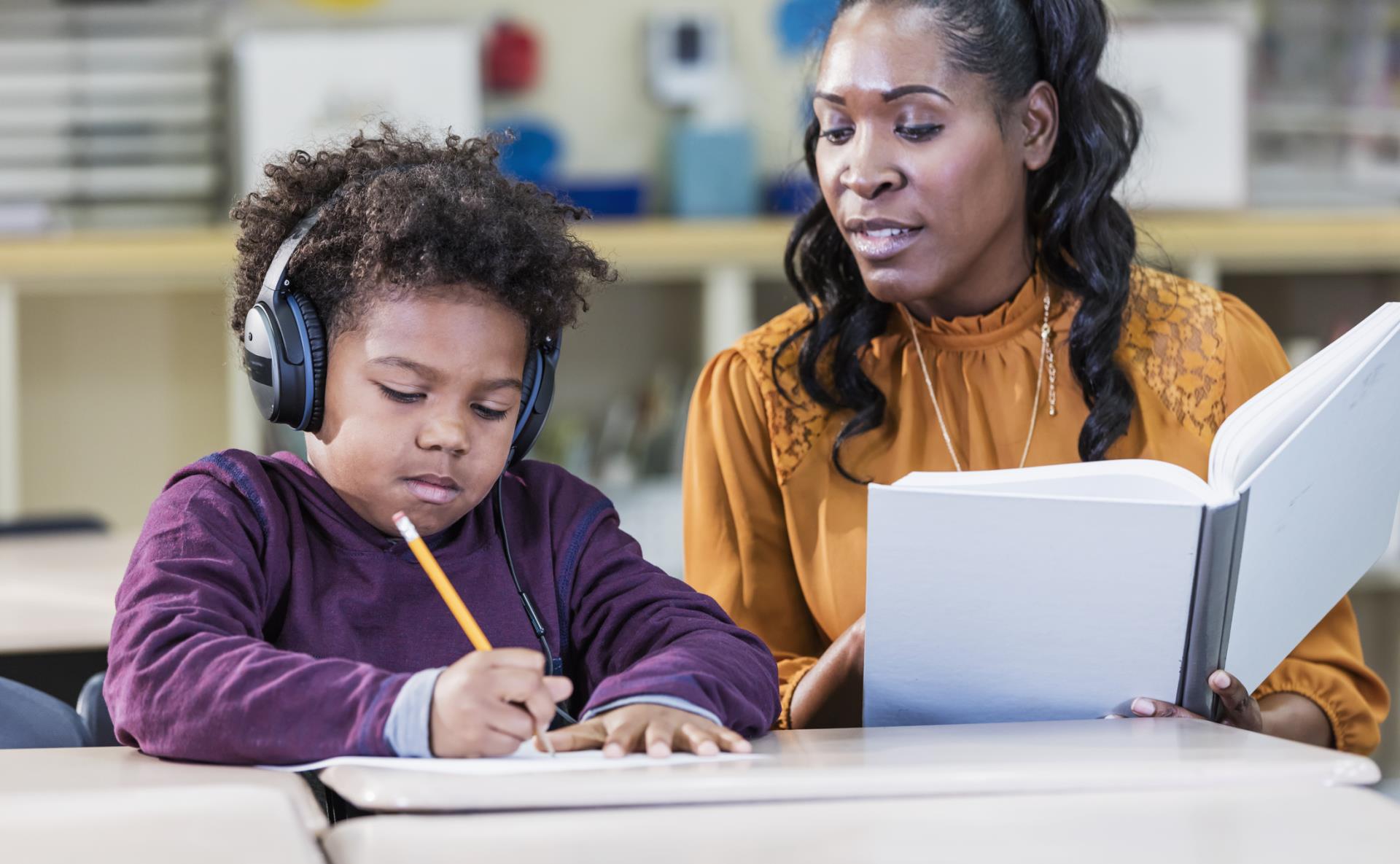 elementary student wearing headphones working with their teacher