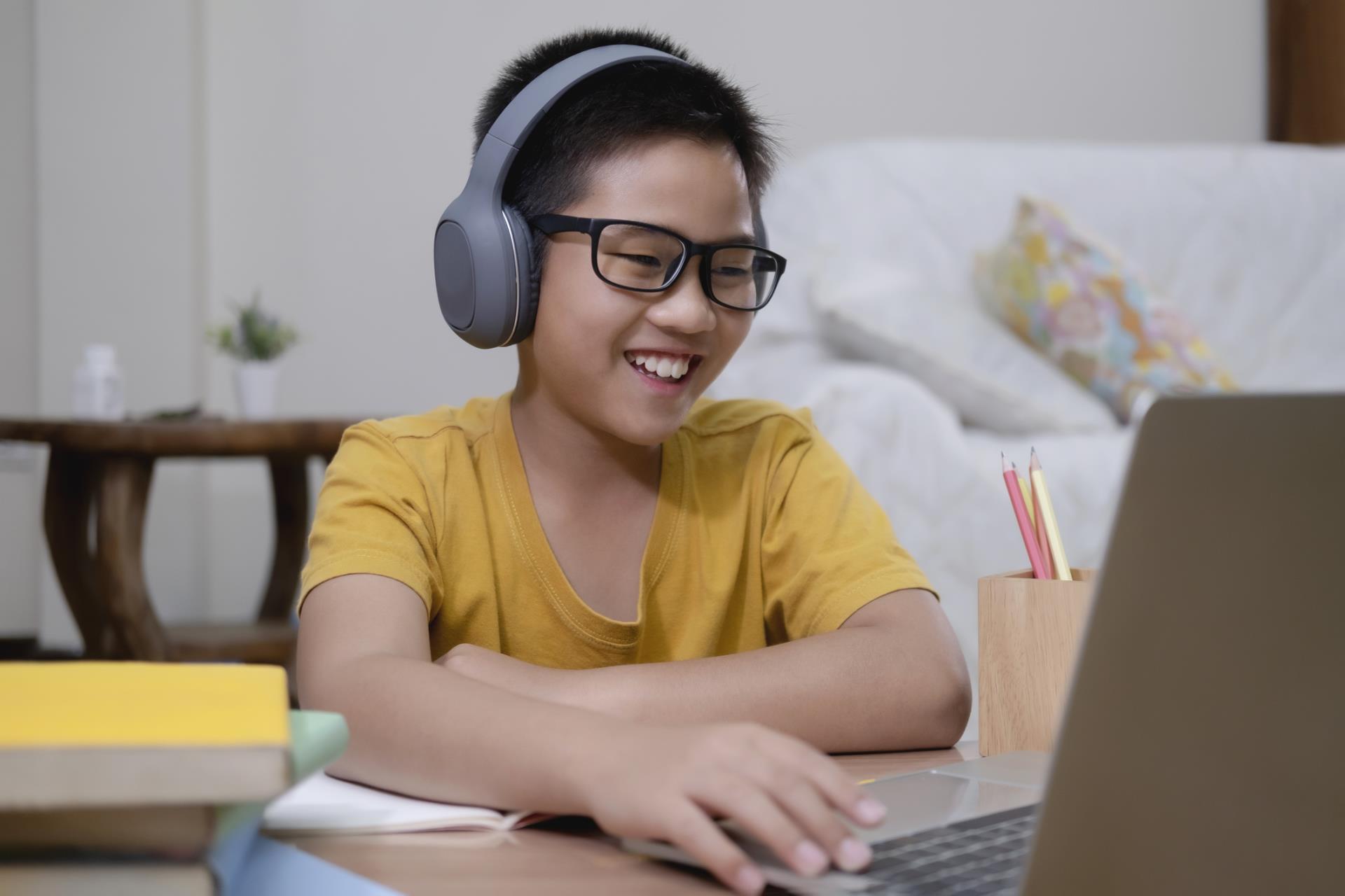 Middle school student wearing headphones and smiling at their laptop while participating in a virtual lesson.