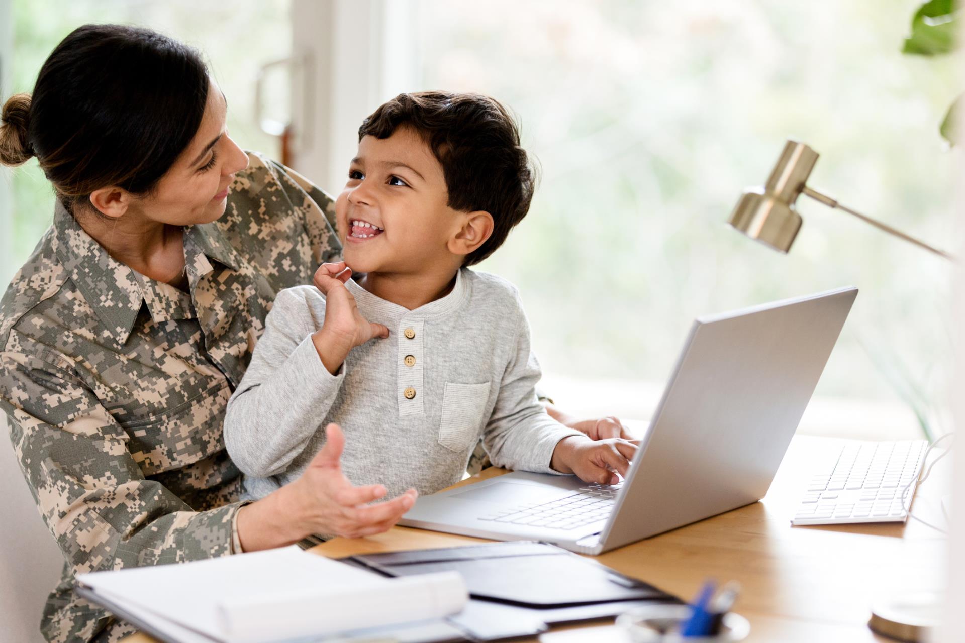 Military parents works with child on their laptop at the kitchen table.