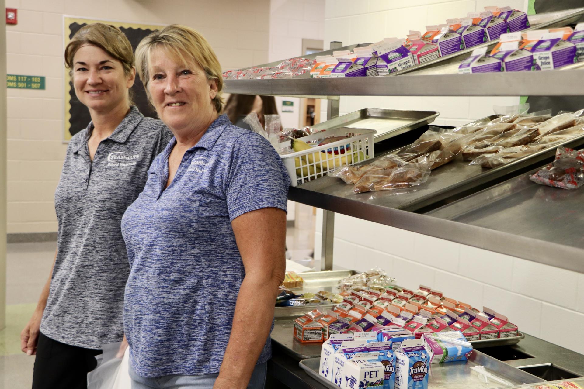 School nutrition professionals stand by breakfast kiosk.