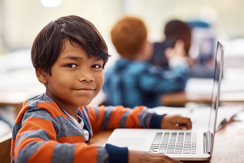 Smiling elementary student working on laptop in classroom
